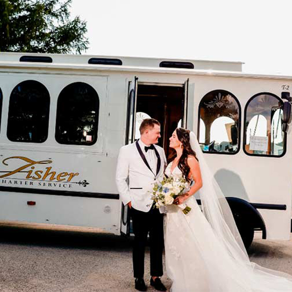 married couple in front of a white trolley by Fisher Bus Inc