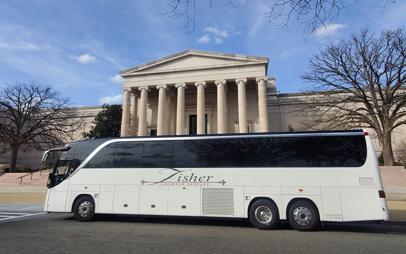 large white charter bus in front of a monument by Fisher Bus Inc in New England